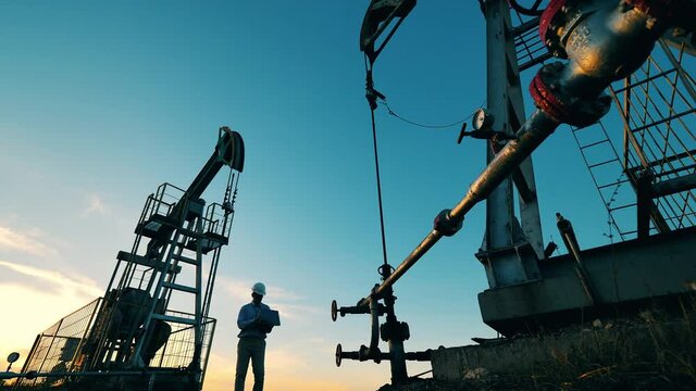 Oil worker inspecting two crude oil pump jacks