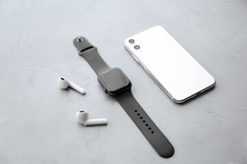 Stylish smart watch, phone and earphones on grey stone table