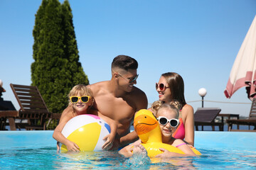 Happy family with inflatable ring and ball in outdoor swimming pool on sunny summer day