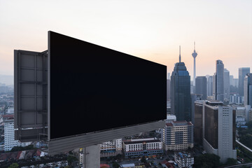 Blank black road billboard with KL cityscape background at sunset. Street advertising poster, mock up, 3D rendering. Side view. The concept of marketing communication to promote or sell idea.