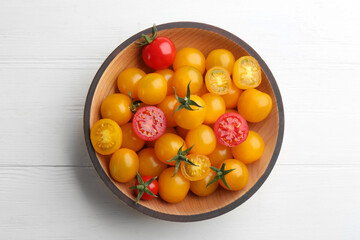 Ripe red and yellow tomatoes in bowl on white wooden table, top view