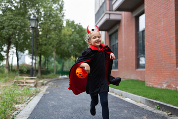 Little Girl in costume of devil with red horns in park. Happy Halloween concept