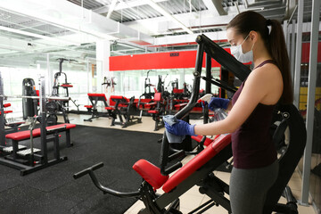 Woman cleaning exercise equipment with disinfectant spray and cloth in gym