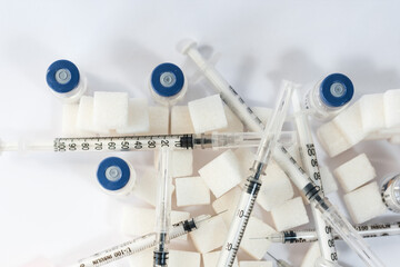 Sugar addiction, insulin resistance, unhealthy diet, sugar cubes pyramid, bottles of insulin and syringe for vaccinationon white background, diabetes protection medical concept, top view.