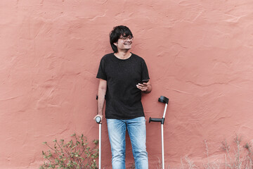 Portrait Of Happy Young Man Using Crutches and phone