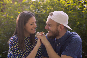 Beautiful young couple is holding hands and smiling while resting in park.