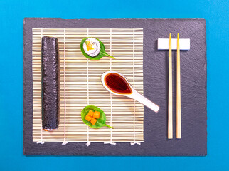 Présentation de plat de cuisine Japonaise, sushi et maki sur fond noir avec sauce soja et baguettes.	