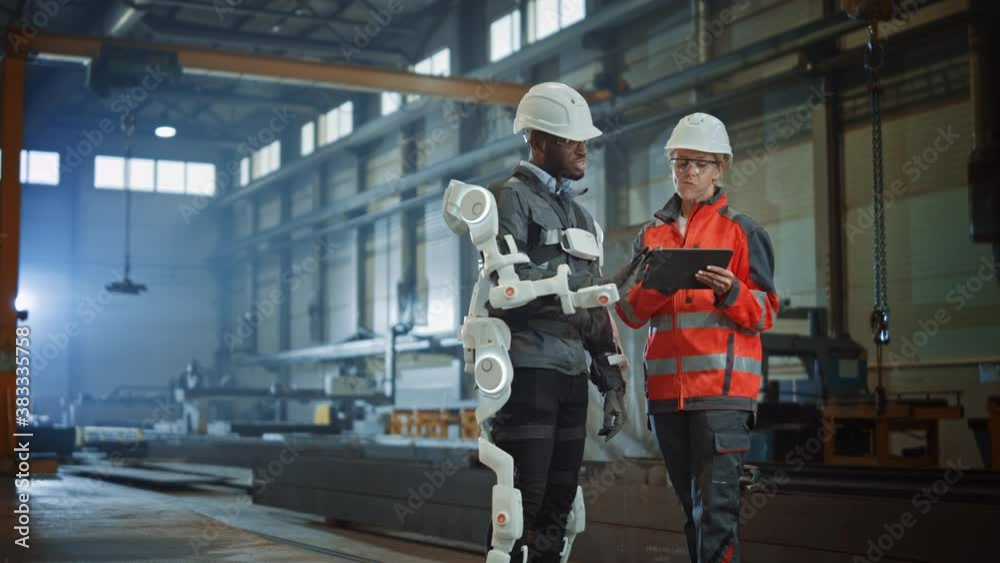 Leinwandbilder Futuristic Concept of a Manual Labor Worker in a Bionic Exoskeleton Prototype Working in a Factory. Heavy Industry Engineer Monitors the Powered Suit on an African American Assistant.