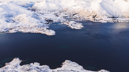 Breathtaking bird's eye view of fjord mountains covered with snow in winter. Aerial top view of scenery rock peaks, picturesque beautiful nature landscape. Lofoten Island surrounds by Nordic sea.