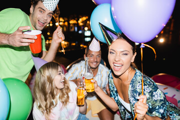 Selective focus of woman holding beer bottle and balloon during party with friends at night