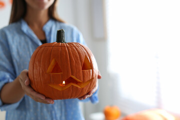 Woman holding pumpkin jack o'lantern indoors, closeup with space for text. Halloween celebration