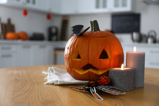 Pumpkin jack o'lantern, candles and Halloween decor on wooden table in kitchen, space for text