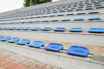 Lots of empty seats in the stadium. Texture of blue chairs. Plastic seats are arranged in a row. Dirty and scratched fan seats.Stadium after rain