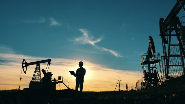 Oil worker walking across an oilfield with his laptop. Oil industry, crude oil prices concept.