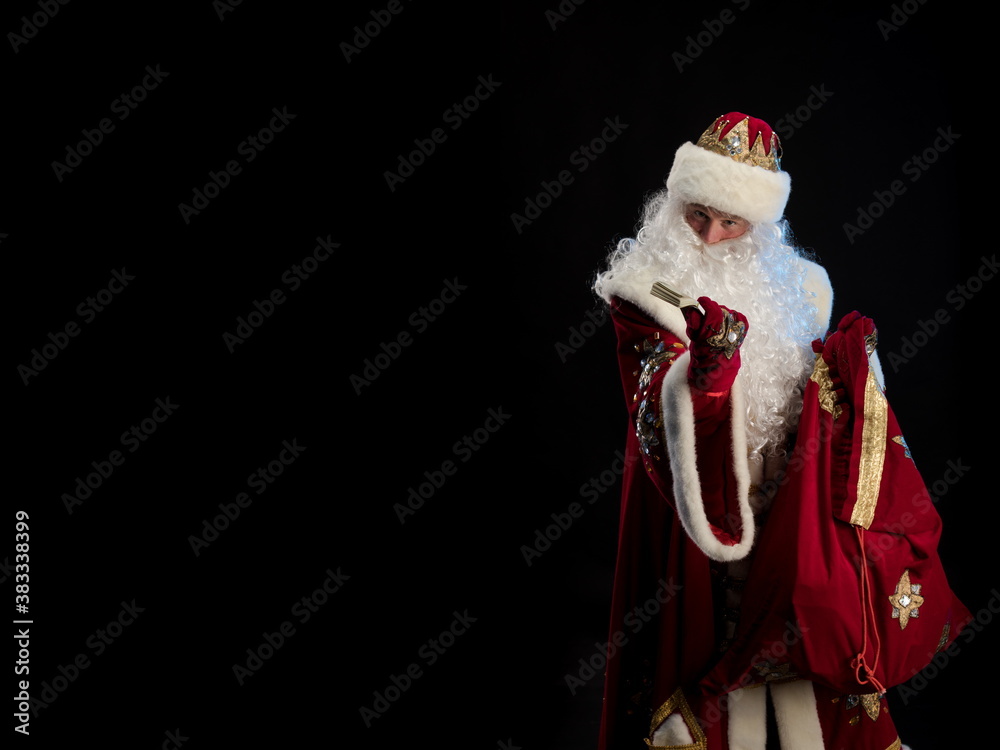 Wall mural Santa Claus in a red fur coat, with a white beard posing on a black background