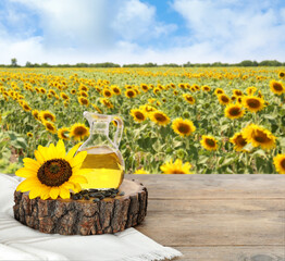 Sunflower oil and seeds on wooden table near blooming field. Space for text