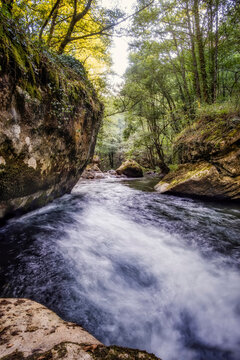 mountain river flowing between large rocks and trees, rio Lor, Poza das Moulas in Ferreiros de Abajo, Sierra do Courel in Lugo, Galicia Spain, vertical