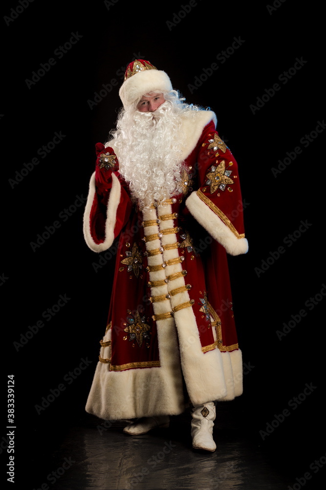 Wall mural Santa Claus in a red fur coat, with a white beard and a bag of gifts posing on a black background