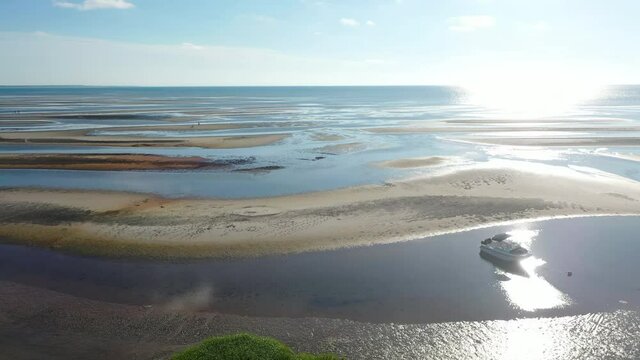 Beautiful Cape Cod Bay Aerial Drone Footage of Bay Side Beach at Low Tide with People, Sand Dunes and a Boat Flying Towards Sun Over The Ocean, Reveal Shot