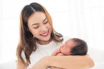 Obraz na płótnie Canvas Pretty asian woman smile and holding a newborn baby in her arms. Happy family. Asia mother lifting and looking her adorable infant baby on white. love people concept