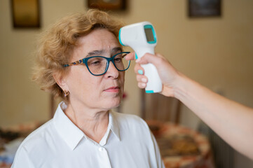 The doctor measures the temperature of an elderly woman with a non-contact infrared thermometer
