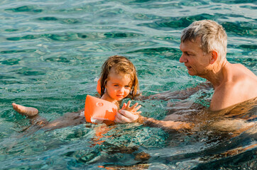 Grandfather teaching toddler girl swimming in sea