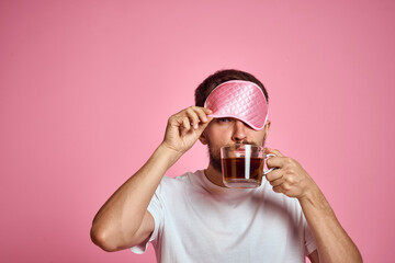 A man in a pink sleep mask with a cup of tea in his hands on an isolated background cropped view
