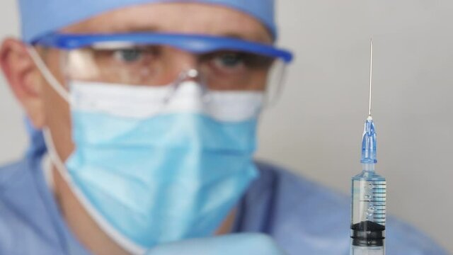 Doctor with syringe. A medical solute in the hands of the doctor. Doctor in the medic face mask is preparing an injection. Close up view