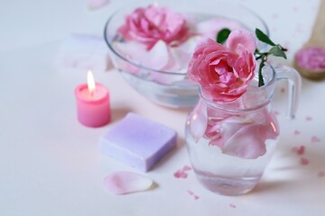 Obraz na płótnie Canvas Fresh pink roses, water, petals, candles on a light background, body care products, natural home cosmetics, healthy lifestyle, alternative medicine