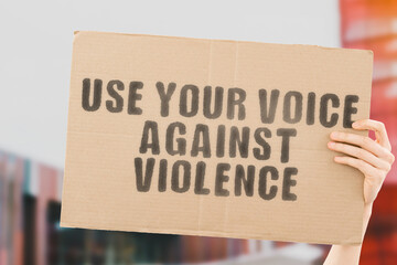 The phrase " Use your voice against violence " on a banner in men's hand with blurred background. Freedom. Equality. Human rights. Protest. Movement