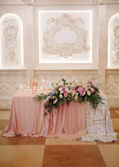 Wedding party. Newlywed's table decorated with tender pink roses, tablecloth, candles and elegant floral composition. Stylish decoration on table.