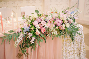Wedding party. Newlywed's table decorated with tender pink roses, tablecloth, candles and elegant floral composition. Stylish decoration on table.