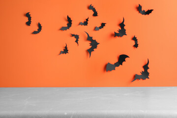 Empty grey table near orange wall decorated with paper bats. Halloween celebration