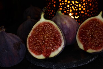 View on isolated raw ripe fig half with group of figs  on black slate stone illuminated by oriental...