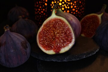 View on isolated raw ripe fig half with group of figs  on black slate stone illuminated by oriental...