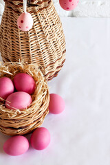 Fototapeta na wymiar Easter composition with decorated tree branches in a wicker vase and pink colored eggs in wicker basket