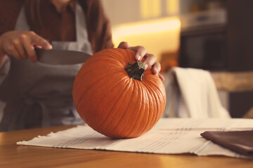 Woman carving pumpkin at table in kitchen. Halloween celebration