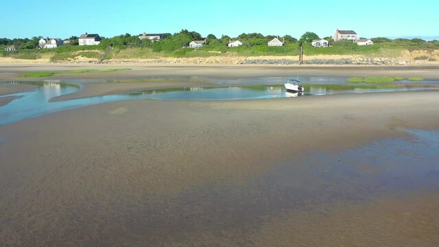Cape Cod Bay Aerial Drone Footage of Bay Side Beach at Low Tide Flying Towards Beach Front Houses with People and Beached Boat