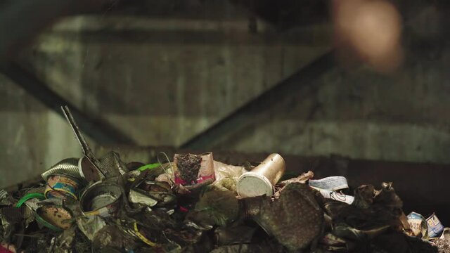 Static shot of a garbage heap of metal waste with cans dropping on it.