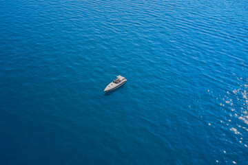 White big boat with awning mooring on blue water. Drone view of a boat  the blue clear waters. Aerial view luxury motor boat.
