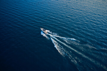 Top view of a white boat sailing to the blue sea.  Yacht in the rays of the sun on blue water.  Aerial view luxury motor boat. Drone view of a boat  the blue clear waters.