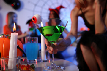 Woman holding cocktail with jelly eyeballs at Halloween party, closeup