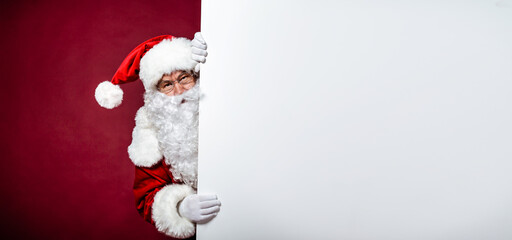 Handsome Santa Claus in glasses and white gloves is holding a big blank board and looking on camera