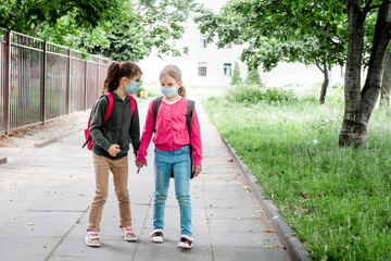 Obraz premium Two girls going back to school during covid-19 pandemic. School child wearing protective face mask in school.