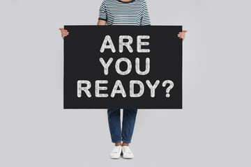 Woman holding poster with text Are You Ready? on light grey background, closeup