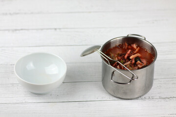 a saucepan of soup, soup ladle and white bowl on white wooden background flat lay