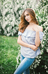 Fototapeta premium A young woman stands by a beautiful Bush with white flowers.The girl's hair is loose.Spring portrait.