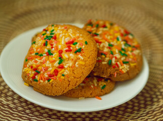 Vanilla cookies with colored sprinkles stacked on a white plate on a knitted tablecloth.