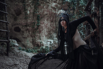 Mysterious sorceress woman witch beautiful black dress walk in gothic forest tree