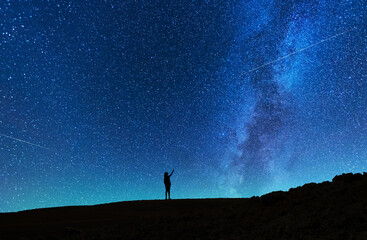 Naklejka na ściany i meble Beautiful starry sky with bright milky way galaxy. Night landscape. Girl silhouette stands on the hill and looking at the starry sky.